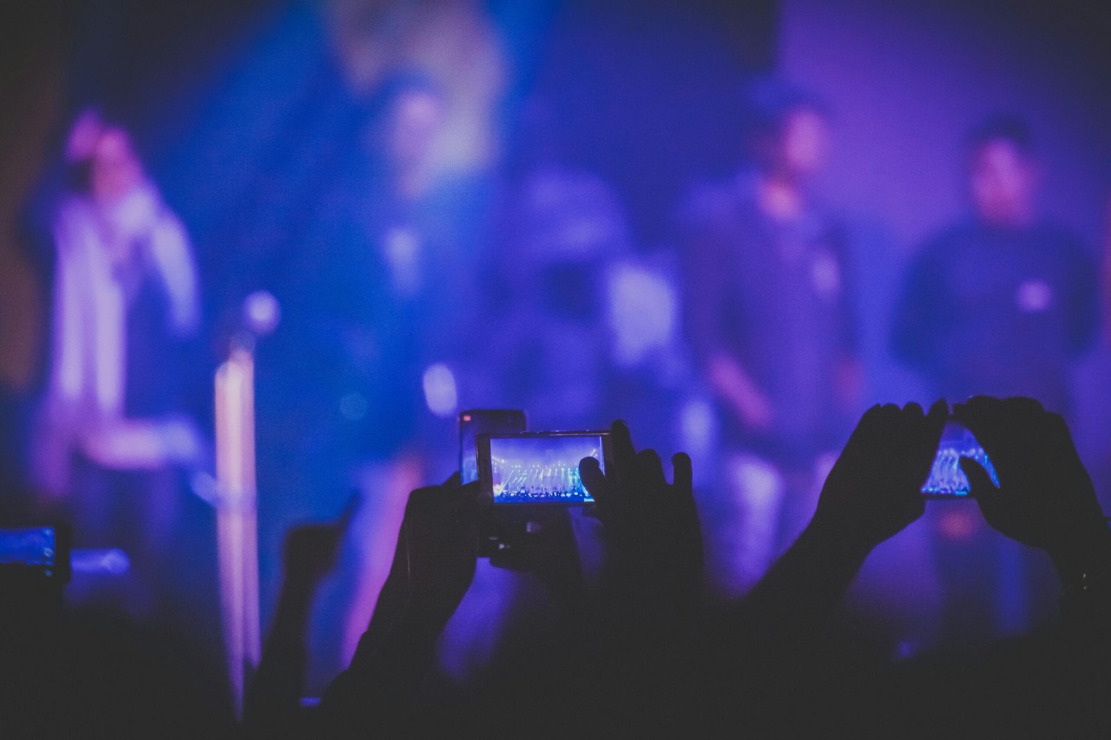A lively concert audience capturing the show with smartphones under vivid stage lights.